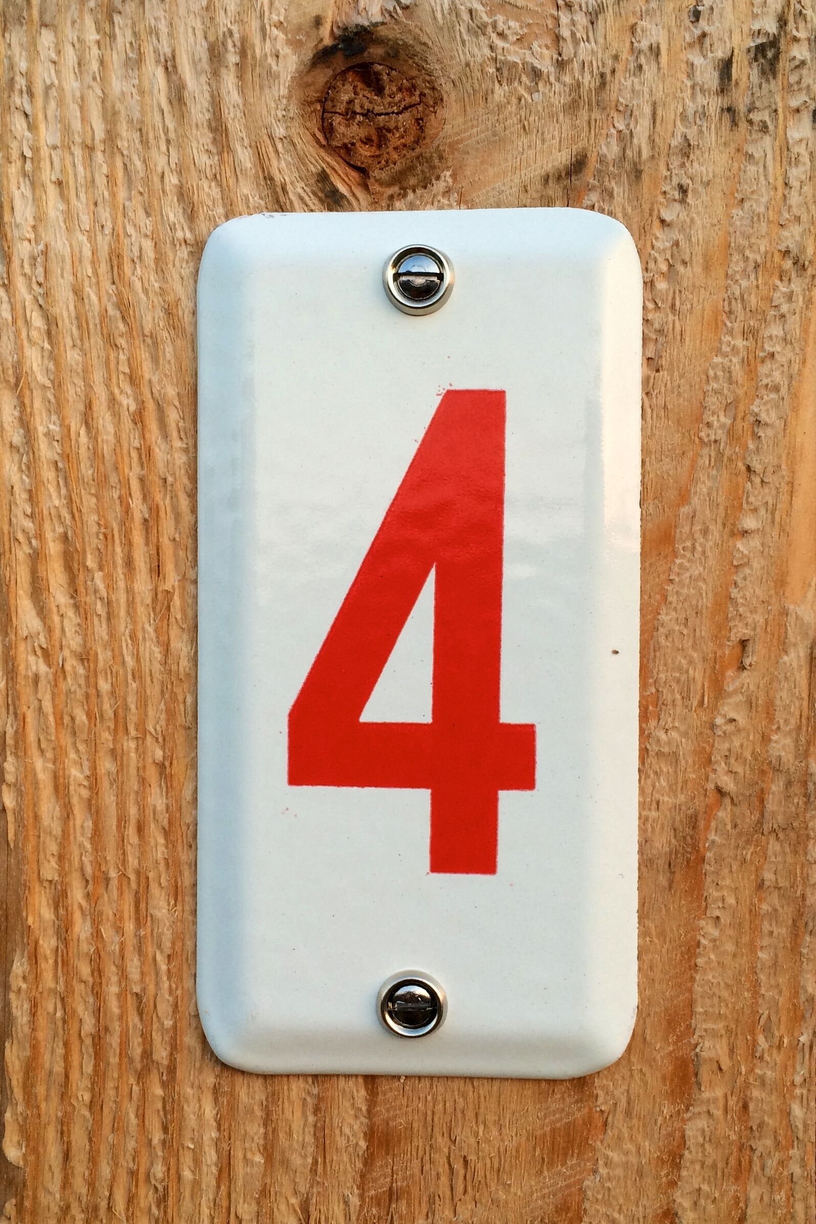 Een wit bord met een rood cijfer '4' bevestigd op een houten oppervlak.