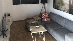 A modern living room with a grey sofa, a small wooden coffee table, and a large painting on the wall.