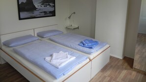 En säng för en person med en sänggavel, ett nattduksbord med en lampa och en inramad bild av en fyr på väggen.