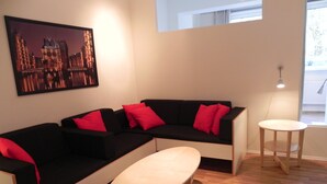 Ett vardagsrum med en svart soffa, röda kuddar, ett vitt soffbord och en tavla som föreställer en stadsbild.