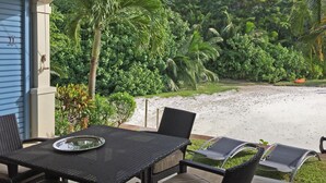 Un espace extérieur abrité, avec une table et des chaises, offrant une vue sur une plage de sable et une végétation luxuriante.