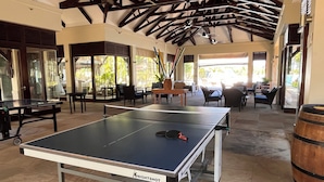 Ein geräumiger Innenbereich mit Tischtennisplatte, bequemen Sitzgelegenheiten und einer hohen Decke mit freiliegenden Balken.