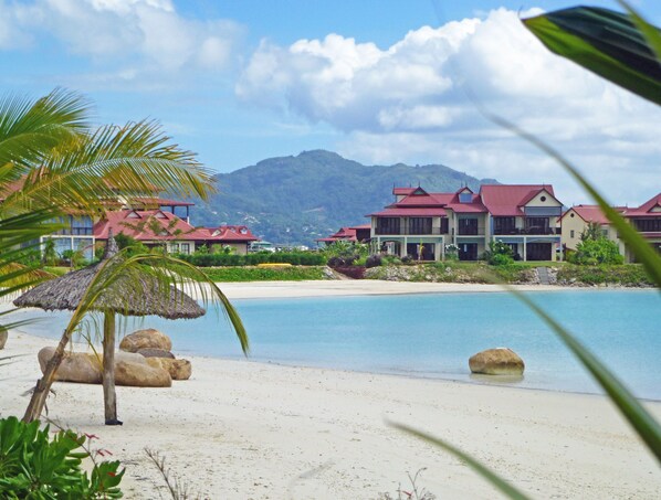 A beachfront hotel with multiple buildings, a sandy beach, and a mountain in the background.