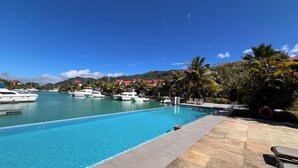 Une piscine d’un bleu éclatant, dotée de chaises longues et offrant une vue sur les yachts amarrés au loin.