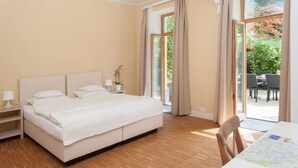 A bedroom with a bed, nightstands, a table with a map, and a view of a garden through large windows.