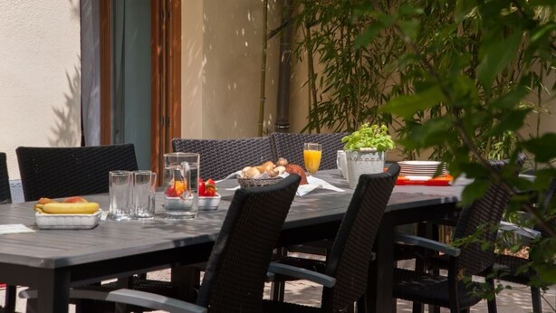 An outdoor dining area with wicker furniture, a table set with fruits, a pitcher, and a glass of orange juice.