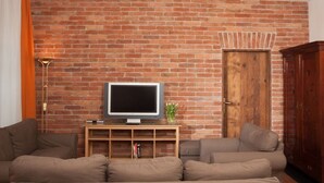 A living room with a brick wall, a television on a wooden stand, and a door.