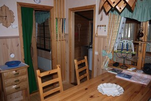 Ein Holzespeisesaal mit Stühlen, einer blauen Schüssel und einem weißen Teller. Ein Holzkasten mit Schubladen und ein grüner Vorhang sind ebenfalls zu sehen.