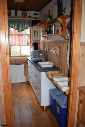 Eine schmale Küche mit Holzausbau, einem Fenster mit grünem Vorhang und einer Heizung.