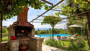 Une cuisine extérieure en pierre, dotée d’une cheminée, d’une piscine et offrant une vue sur la mer.