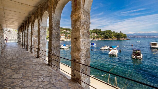 Un sentier dallé de pierres, agrémenté d’arches, un ciel d’un bleu limpide et des bateaux sur une mer calme.