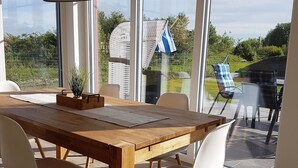 A dining area with a wooden table and chairs, large windows, and a hanging light fixture.