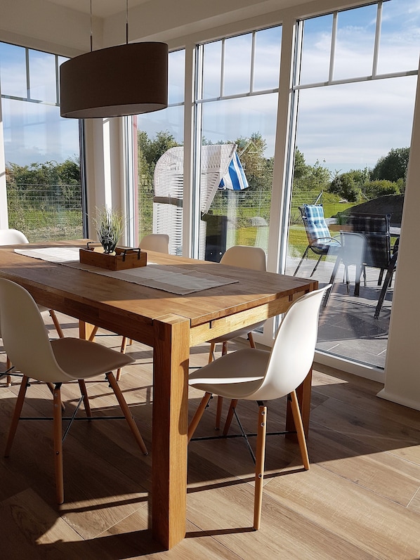 A dining area with a wooden table and chairs, large windows, and a hanging light fixture.