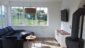 A modern living room with a sectional sofa, a small wooden coffee table, a black fireplace, and a large window offering a view of greenery.