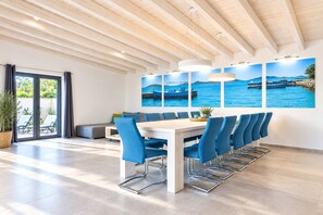 Ein moderner Essbereich mit einem Holztisch, blauen Stühlen und Meerblick durch große Fenster.