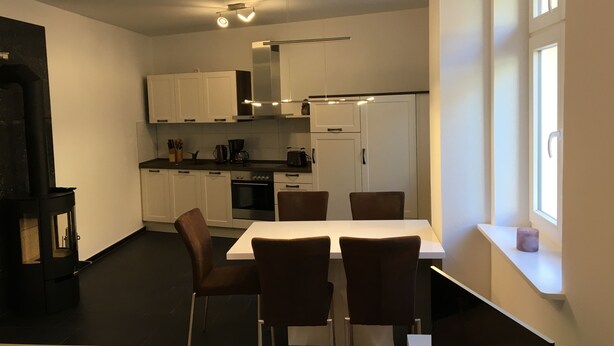 Ett modernt kök med vita skåp, ett matbord med stolar och en svart spis.