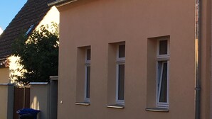 En byggnad med tre fönster, en soptunna och en kullerstensgata.