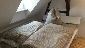 En säng med randigt sänglinne och en kudde med ett stjärnmönster i ett rum med trägolv och ett sluttande tak.