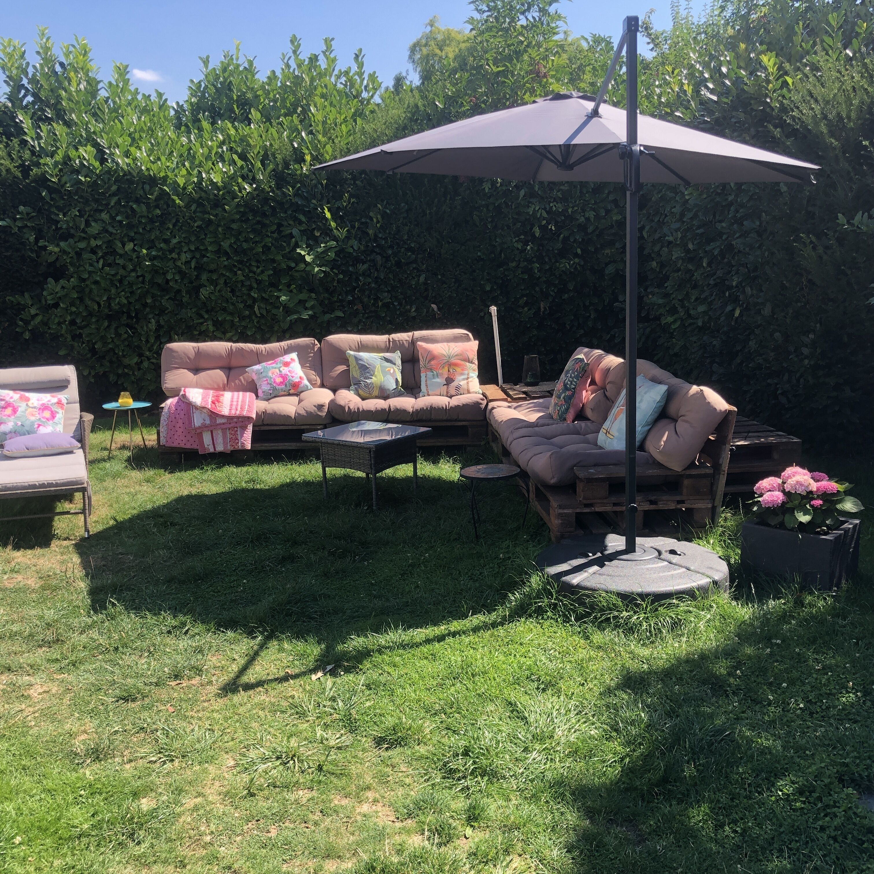 Een terras met een zachte bank, een ronde tafel en een grote parasol voor beschutting.