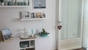 A room with a white console table, a door, and a wall-mounted shelf with decorative items.