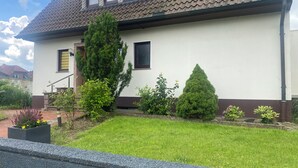 A house with a tiled roof, a front yard with grass, a tall coniferous tree, and a smaller coniferous tree.