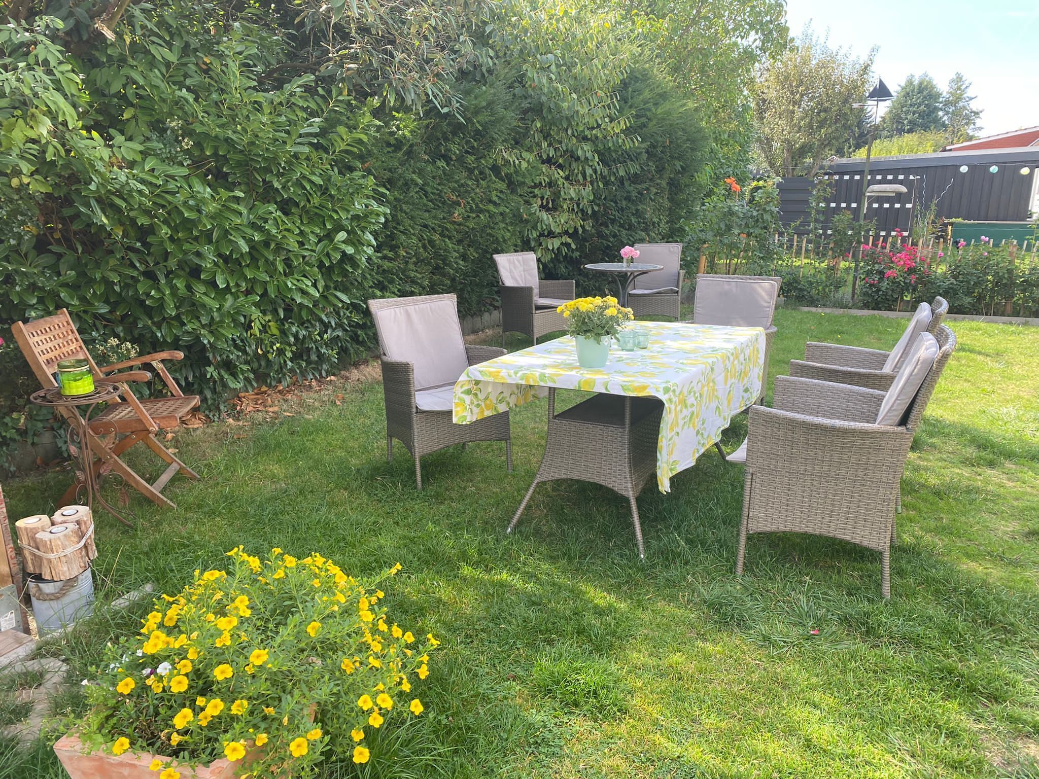 A patio area with wicker furniture, a table with a floral tablecloth, and a potted plant with yellow flowers.