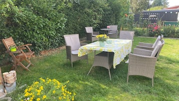A patio area with wicker furniture, a table with a floral tablecloth, and a potted plant with yellow flowers.