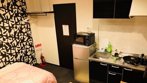 Quarto de hotel pequeno e funcional, com cama, cozinha compacta e banheiro.