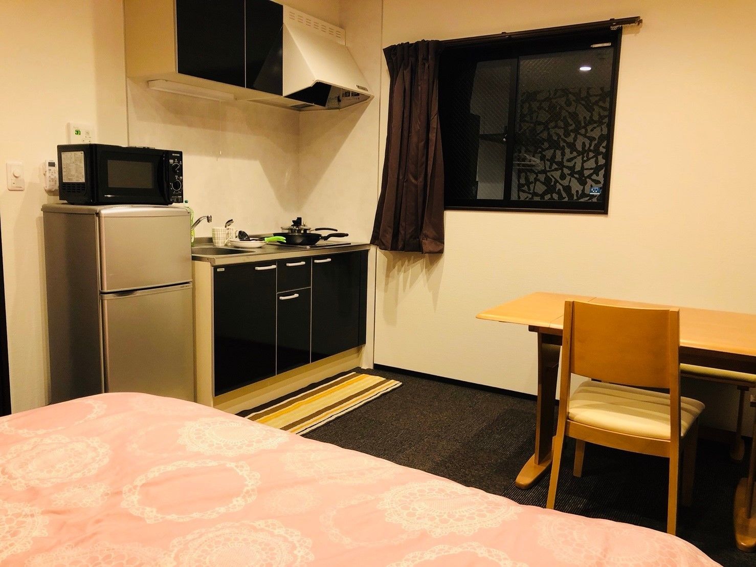 A compact room with a bed, a kitchenette, a small table, and a chair.