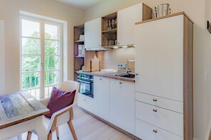 A modern kitchen with white cabinets, a wooden countertop, and a window providing a view of greenery outside.