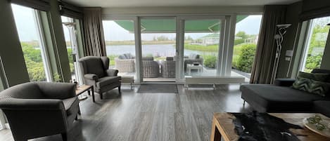 A spacious living room with a large sliding glass door leading to a balcony, furnished with wicker chairs and a sofa.