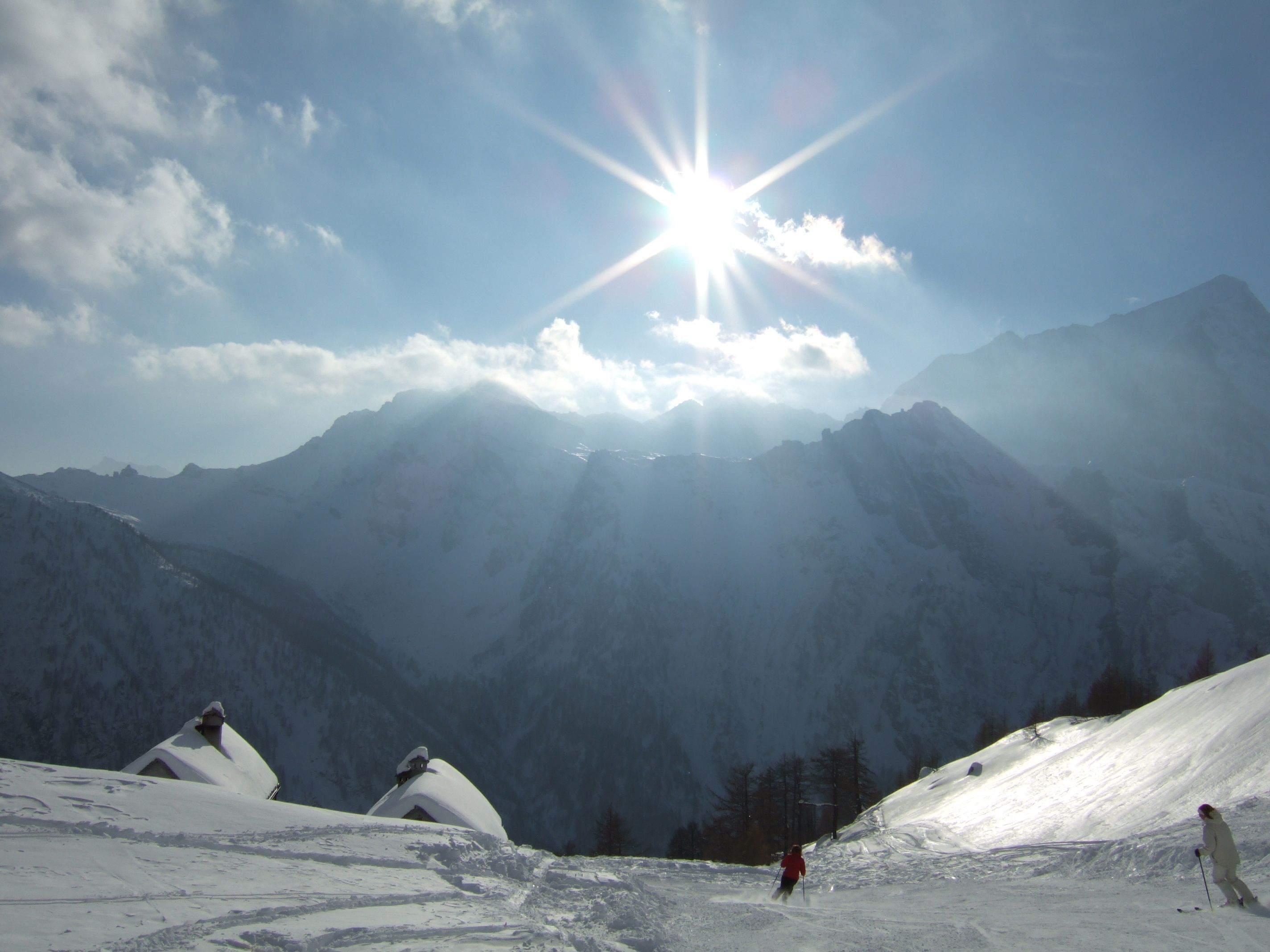 Un paysage de montagne enneigé, avec un ciel dégagé et un soleil brillant.