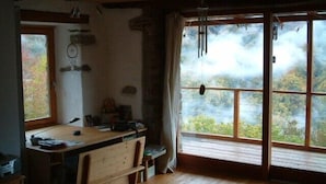 L’intérieur d’un chalet rustique est aménagé avec un bureau en bois, des chaises et une grande fenêtre donnant sur une zone boisée.
