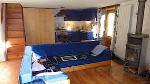 Un salon chaleureux avec un canapé bleu, des meubles en bois, une cuisine aux meubles bleus et un poêle à bois.