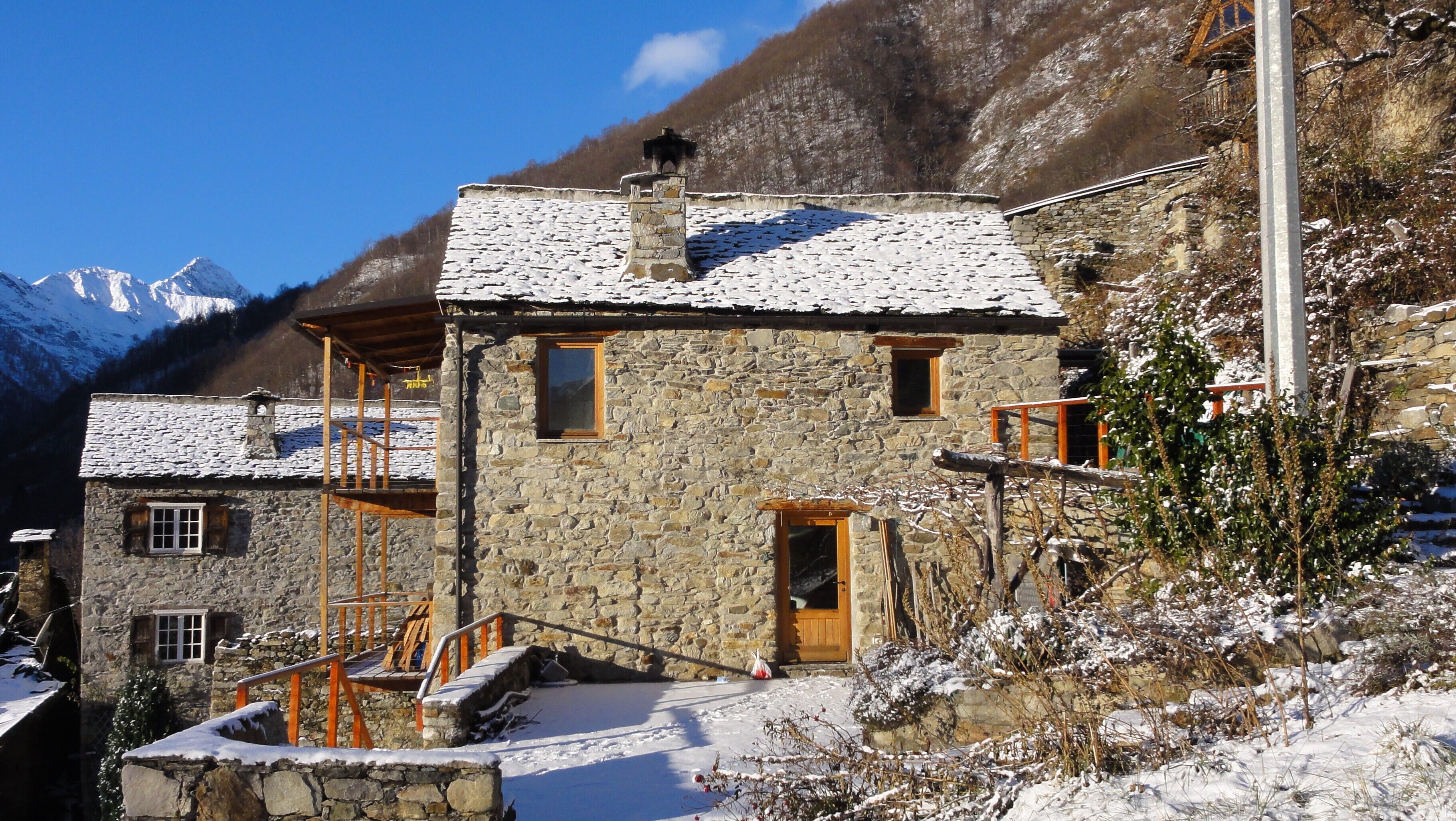 A stone building with a wooden door and windows, surrounded by snow-covered ground and mountains in the background.
