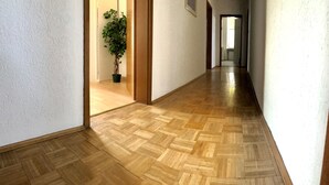 A hallway with wooden parquet flooring, white walls, and a potted plant.