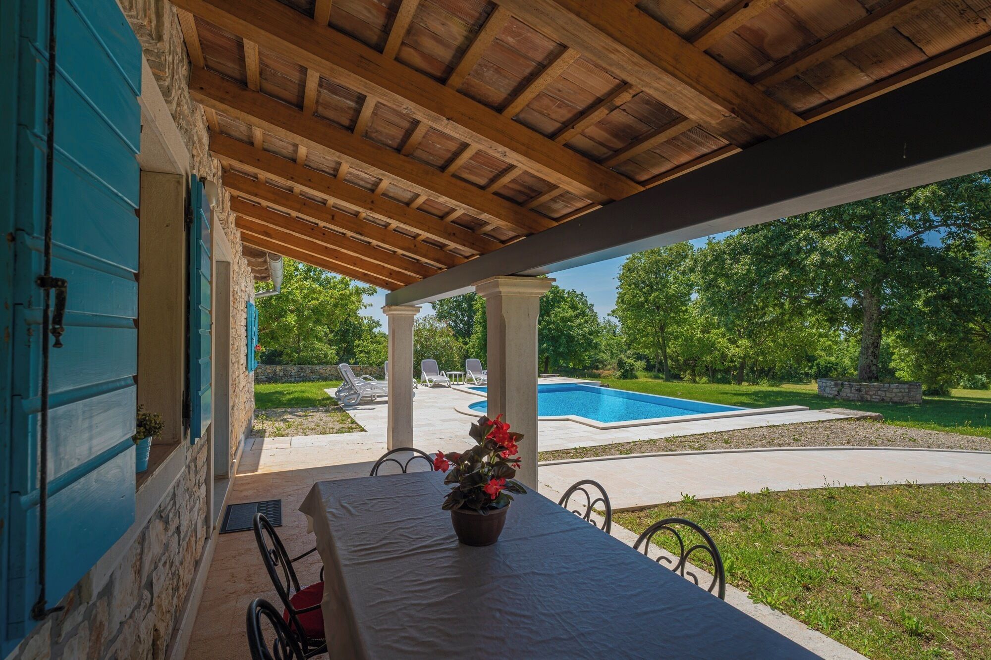A covered outdoor area with a pool, stone walls, and a table with a potted plant.