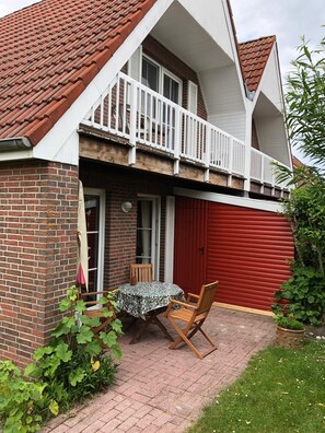 A two-story house with a red garage door, a balcony with white railings, and a brick exterior. - Holiday house in Greetsiel (Greetsiel)