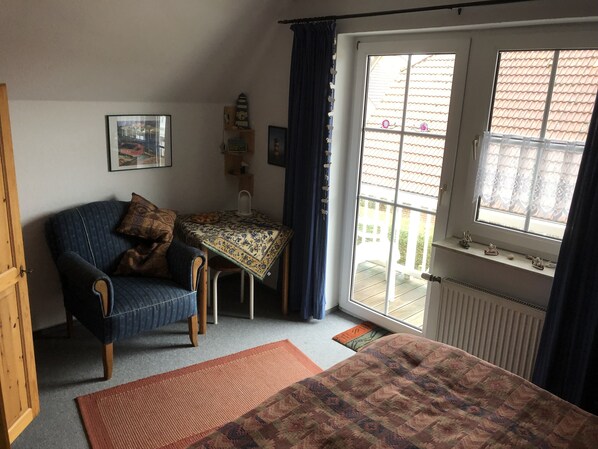 A cozy room with a bed, a chair, a table with a patterned tablecloth, a window with curtains, and a radiator. - Holiday house in Greetsiel (Greetsiel)