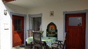 Une terrasse avec une table et deux chaises, une porte en bois et une fenêtre avec un rideau.