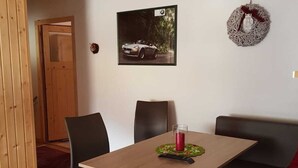 Une pièce chaleureuse avec une table en bois, des chaises noires, une bougie rouge et un tableau représentant une voiture accroché au mur.