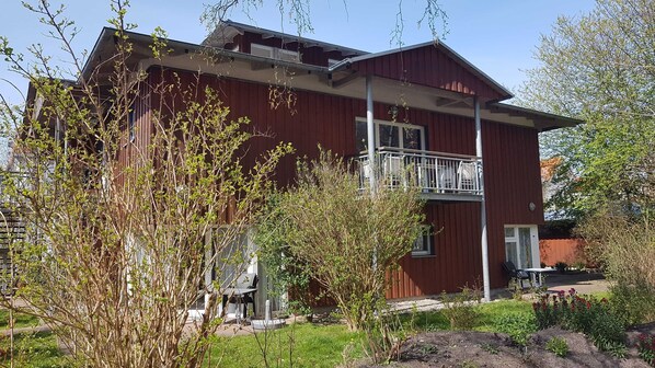 A red building with a balcony, surrounded by greenery and a garden.