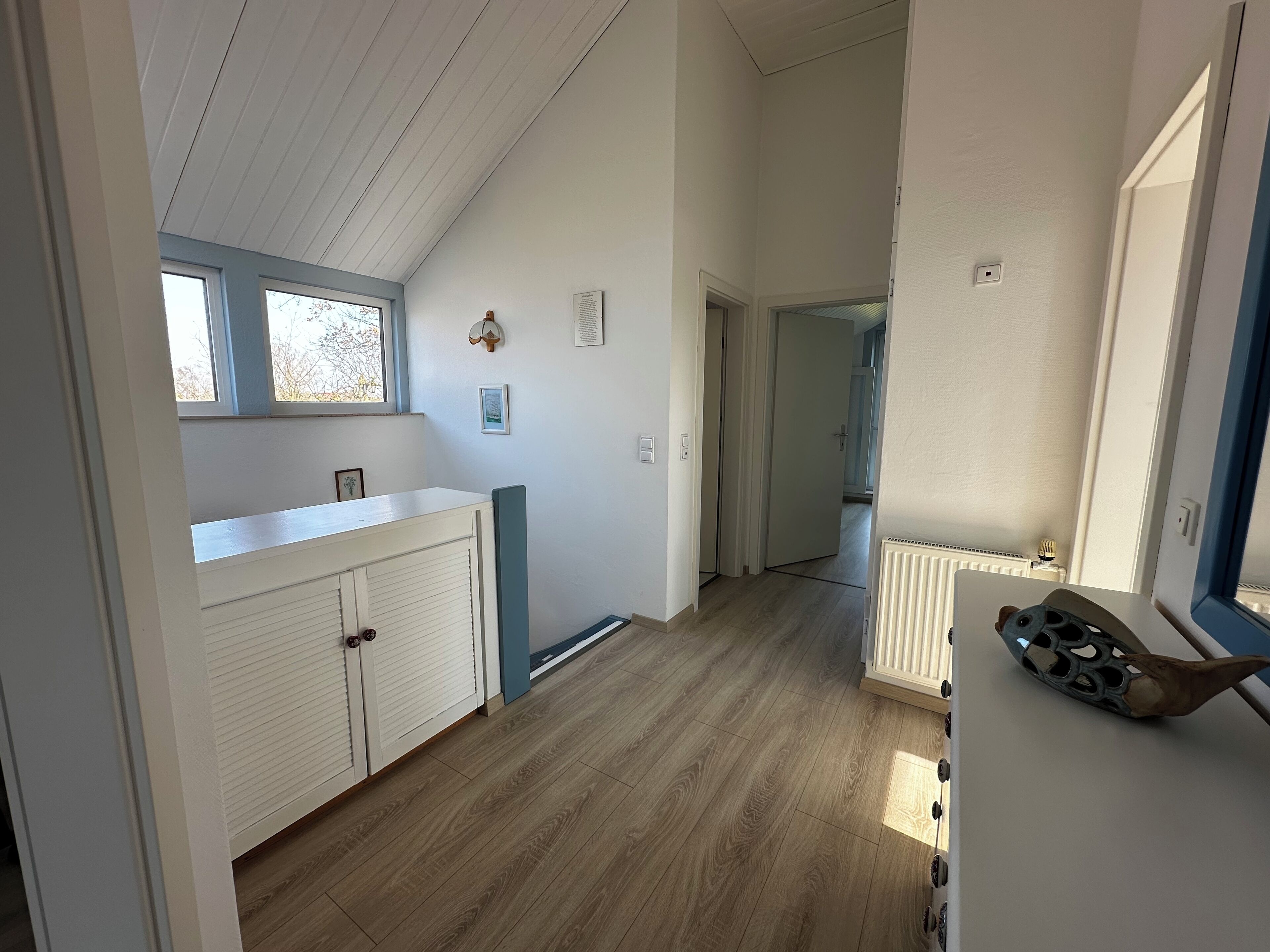 Un couloir étroit avec un plafond en pente, un plancher en bois et un radiateur sur le côté droit.