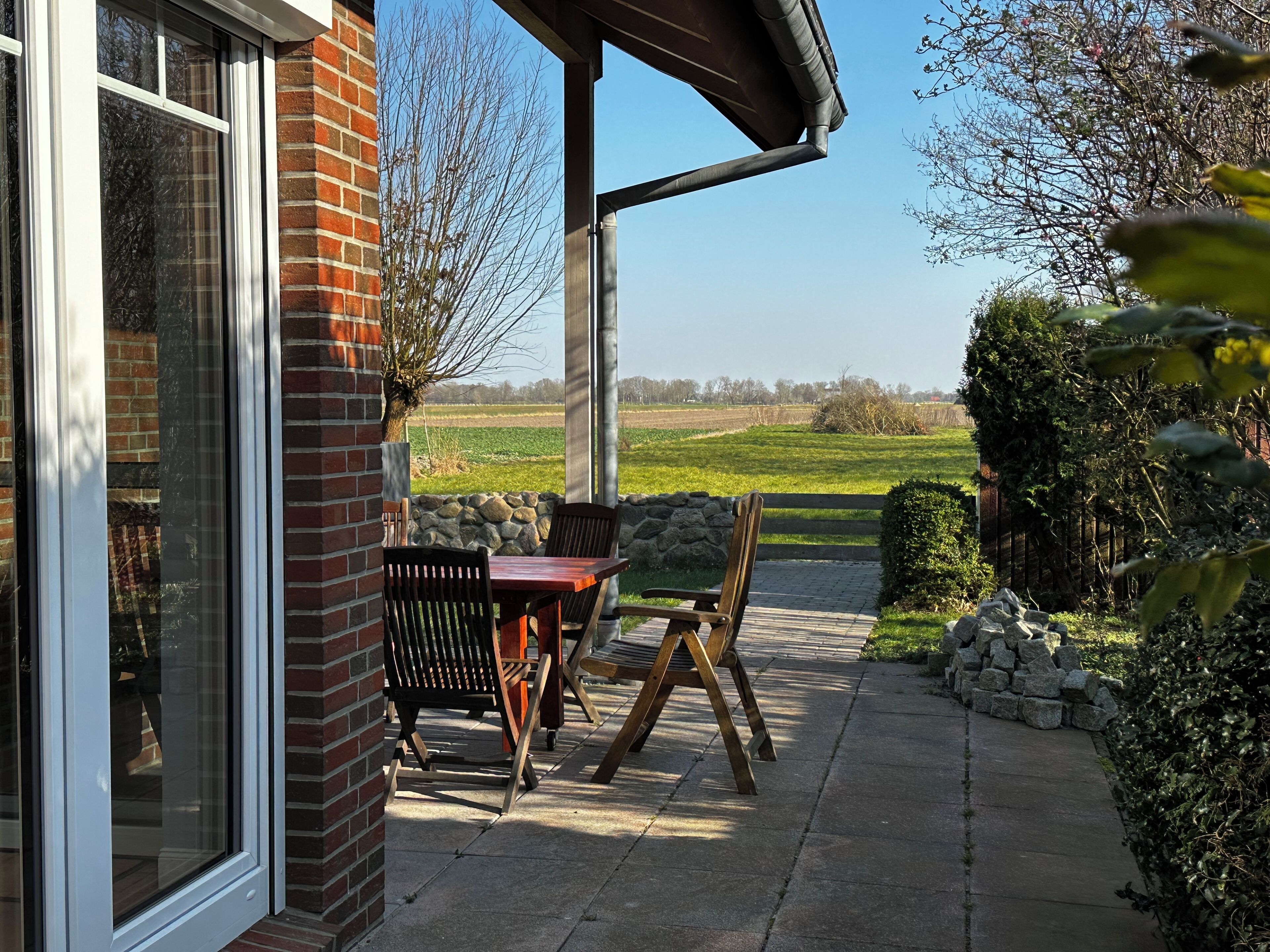 Een terras met een tafel en stoelen, een stenen muur en uitzicht op een veld.