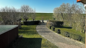 A pathway leading to a building with a green roof, surrounded by well-maintained hedges and trees. - House "NordSeeStern", detached, right on the North Sea dike with a fireplace (Wurster Nordseeküste)