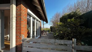 A brick building with a covered patio area, a wooden gate, and a view of the surrounding landscape. - House "NordSeeStern", detached, right on the North Sea dike with a fireplace (Wurster Nordseeküste)