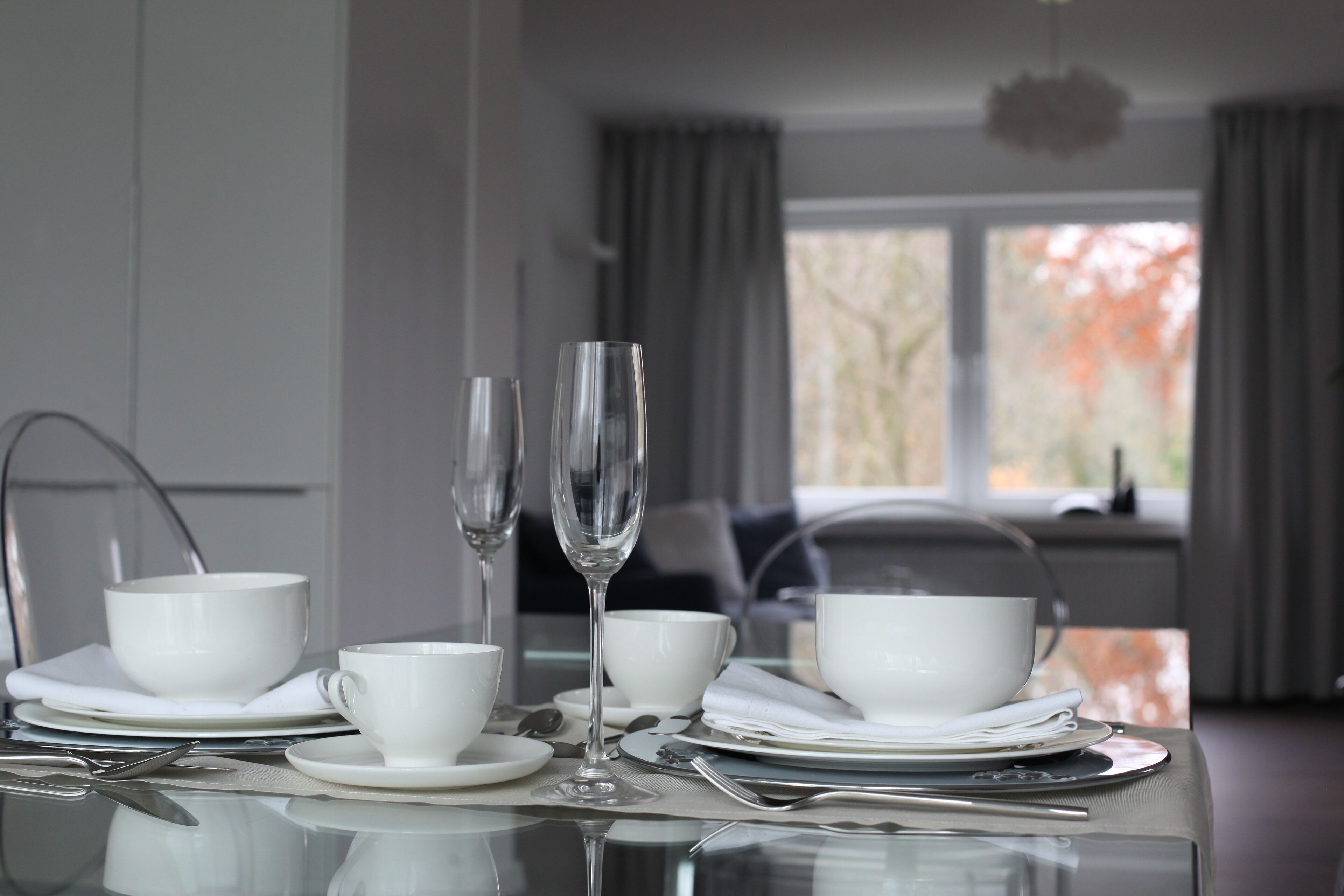 Een eettafel gedekt met witte kopjes, schoteltjes en een glas water.