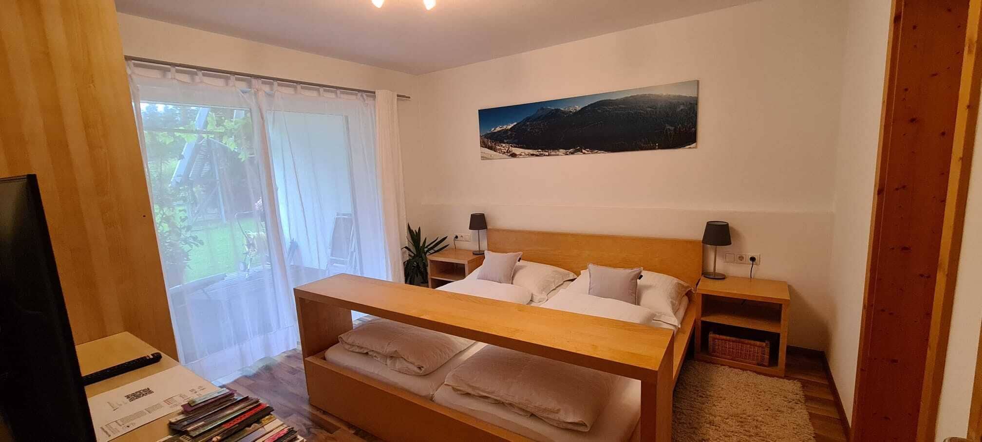 Une chambre avec un lit en bois, une literie blanche, une table de chevet avec une lampe, une fenêtre avec des rideaux légers et un tableau encadré au mur.