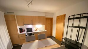 Una cocina compacta con armarios de madera, una mesa de comedor con sillas y un estante de metal negro.