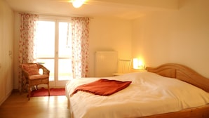 A bedroom with a bed, a chair, a radiator, and a window with curtains. - Exclusive vacation apartment | dream location at the foot of the Alps | suitable for allergy sufferers (Füssen)